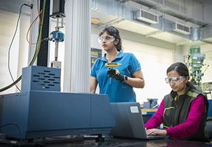 Two women wearing safety glasses, working at a computer