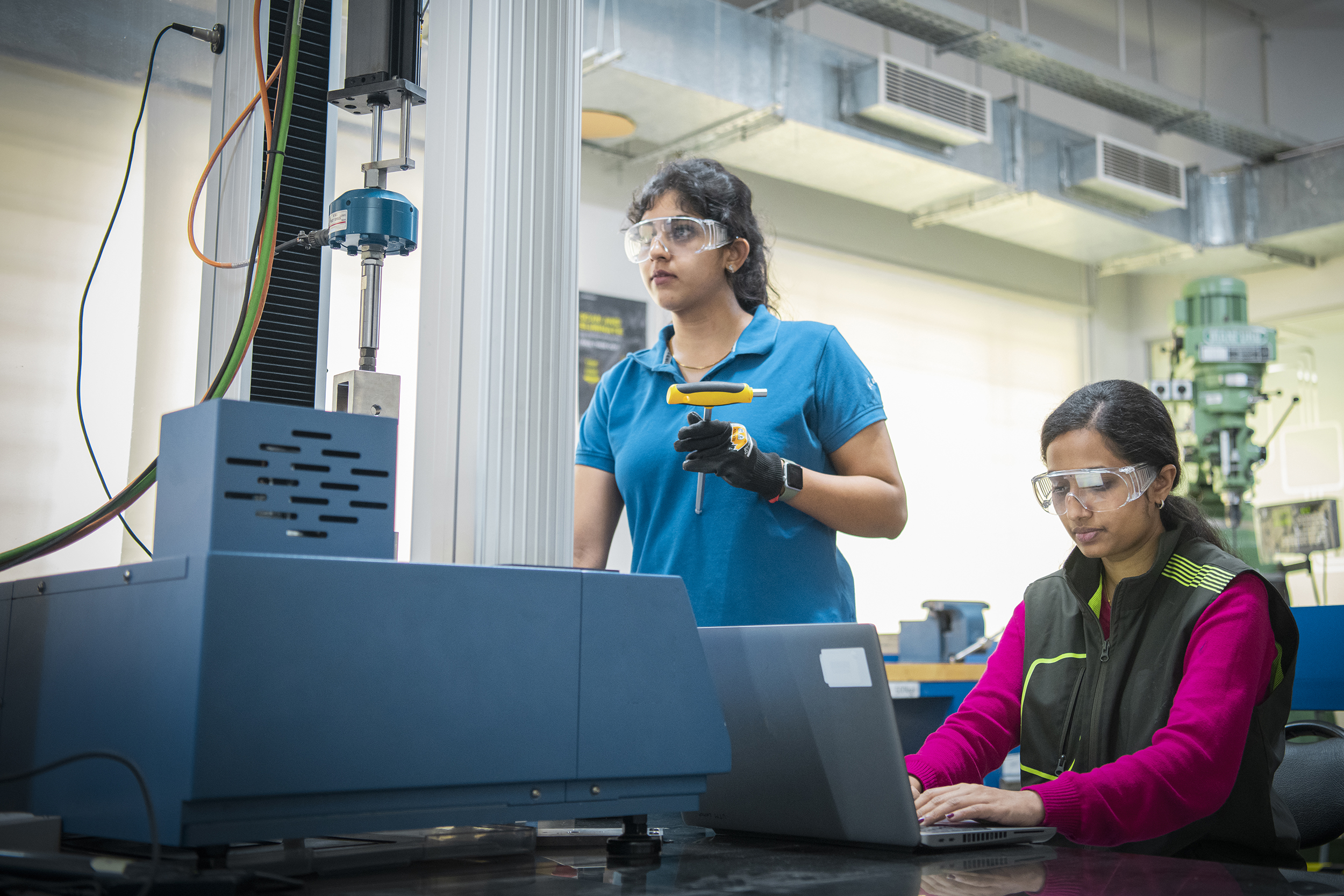 Two women wearing safety glasses, working at a computer